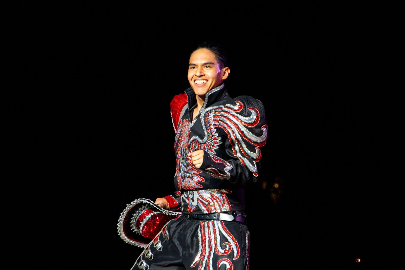 Bailarín con traje de caporal bordado en rojo y plateado sonriendo en el escenario