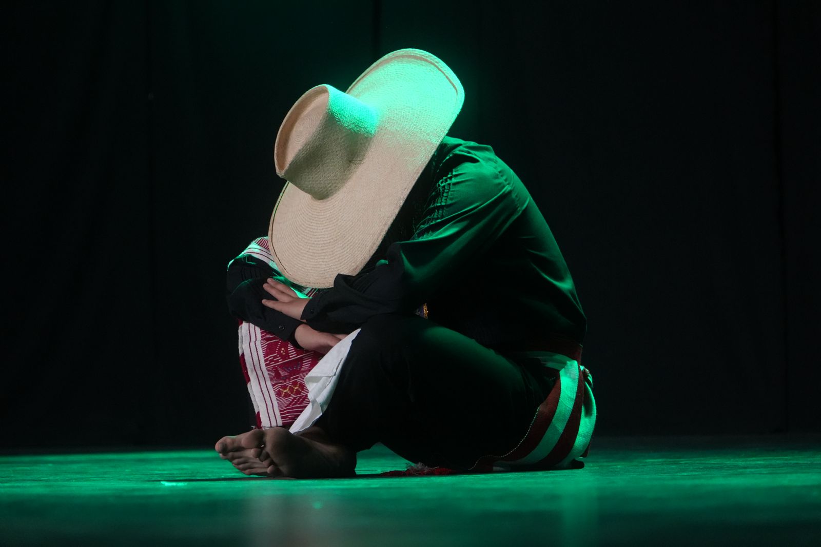 Danzante con traje verde y sombrero alto bajo luces de escenario